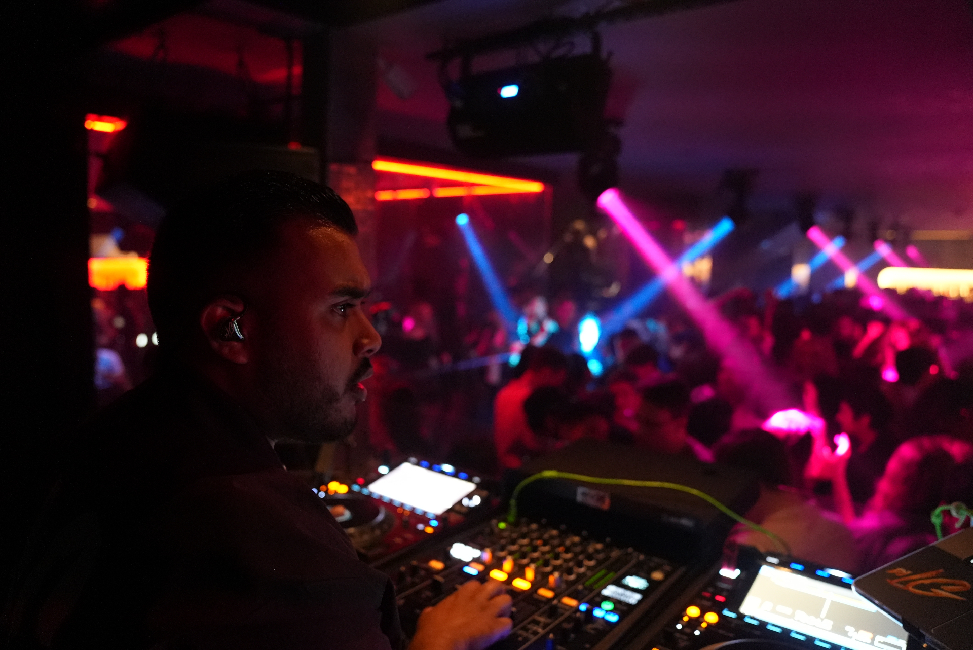 DJ LG performing at a festival, electric orange lasers across a packed crowd